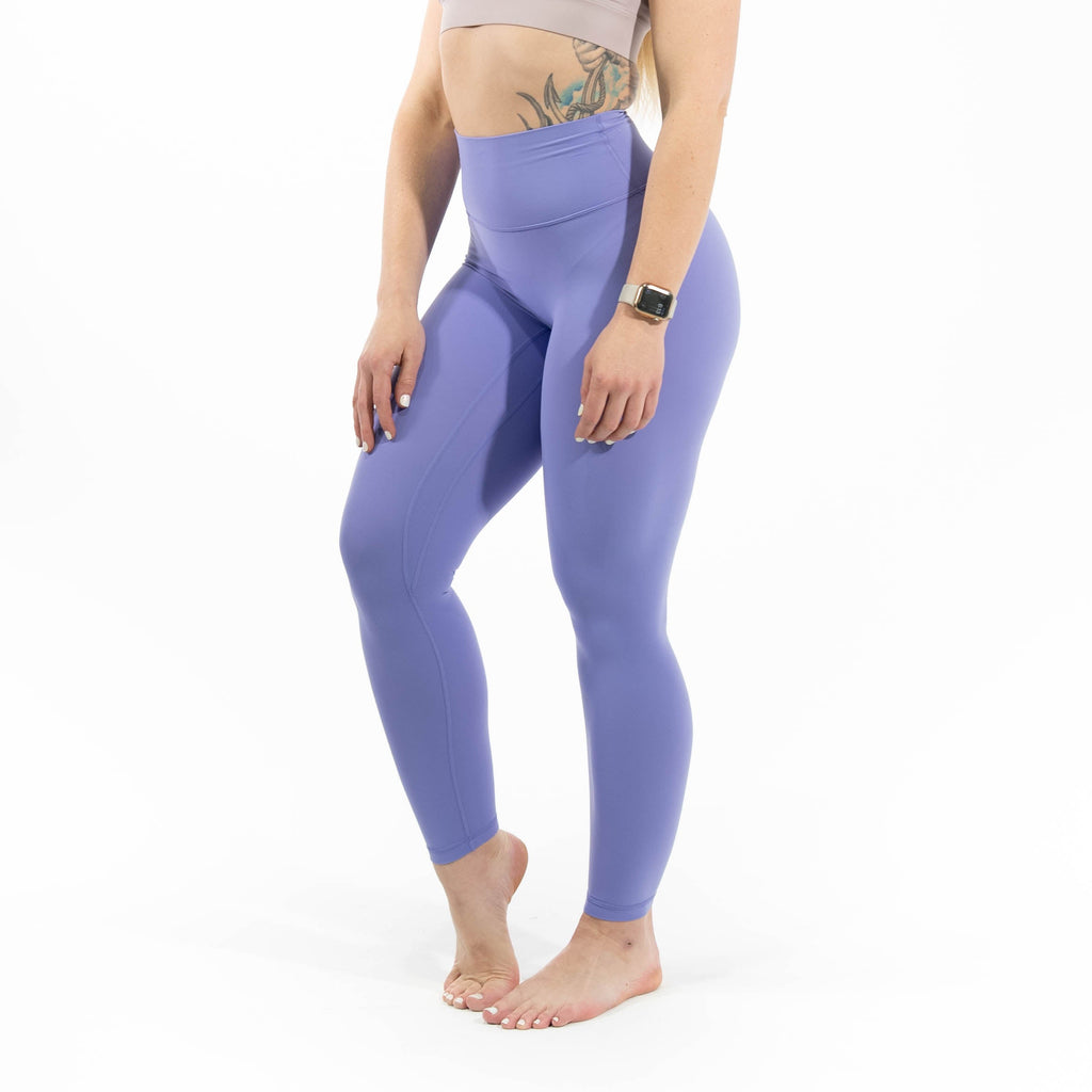 Woman wearing a beige sports bra and purple leggings on a white background