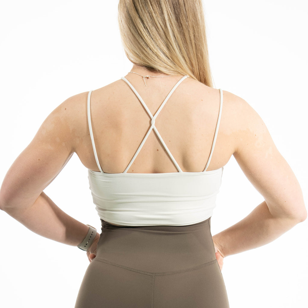 Person wearing a white sports bra and brown leggings on a white background