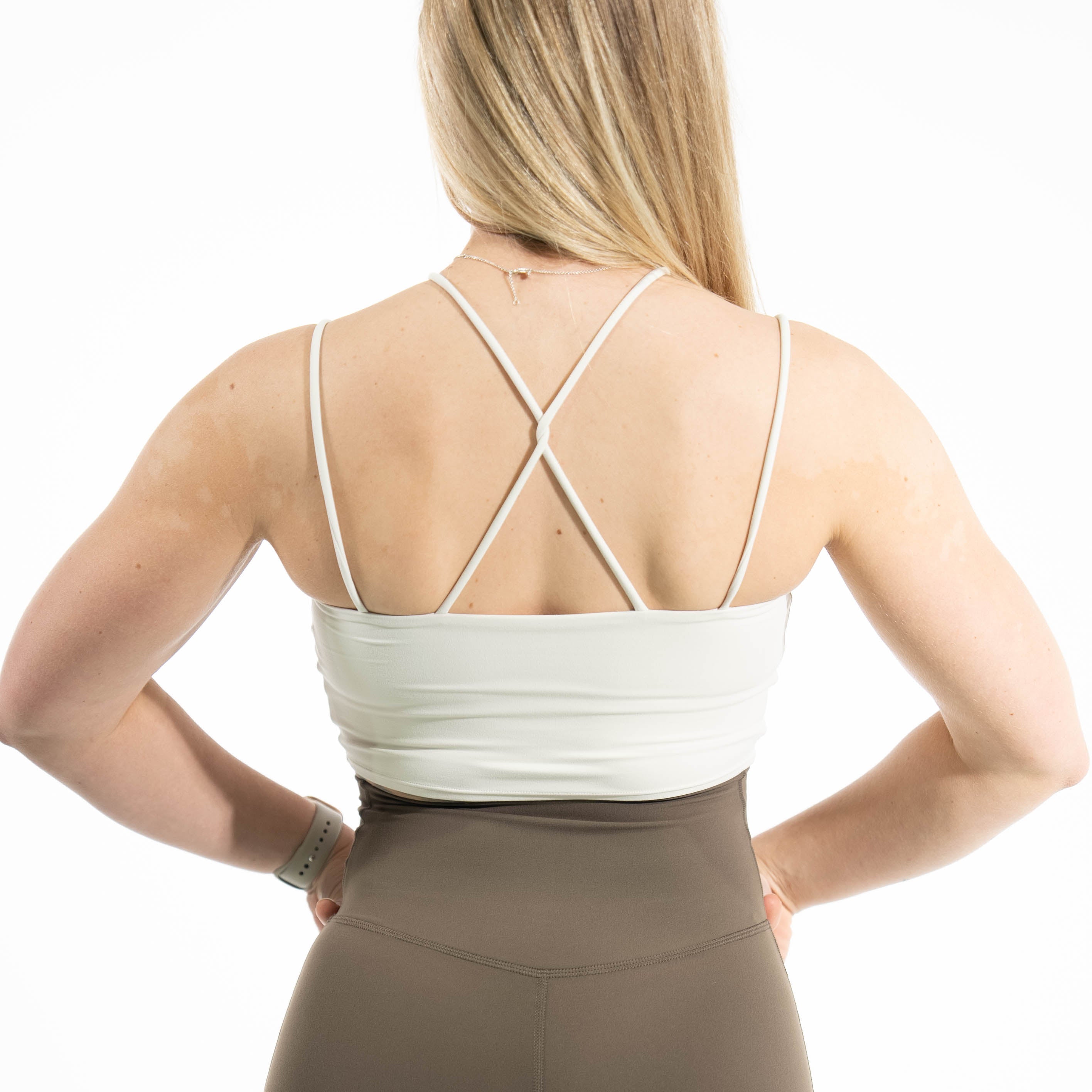 Person wearing a white sports bra and brown leggings on a white background
