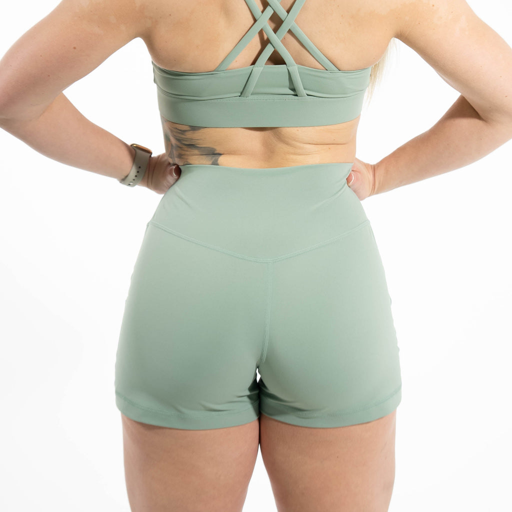 Person wearing a green sports bra and shorts set on a white background